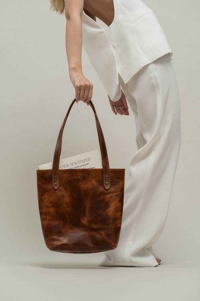 Stylish woman holding a brown leather bag in a minimalist studio setting.