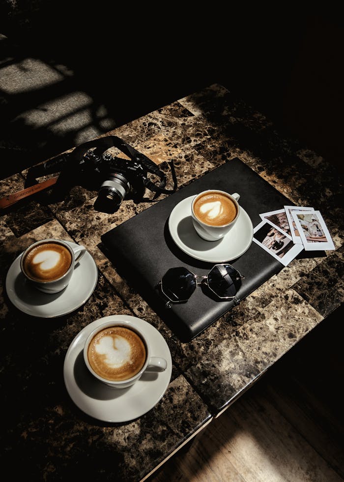 Enjoy a relaxing coffee break with cappuccinos, camera, and laptop on a stylish table.